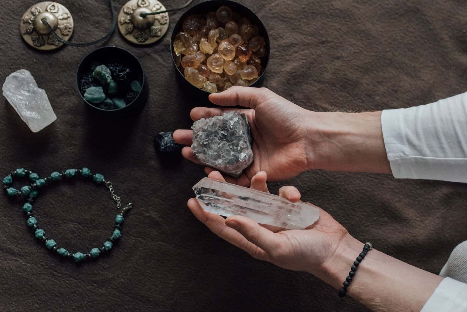 Close-up of hands holding healing crystals, surrounded by natural gemstones and a beaded bracelet.