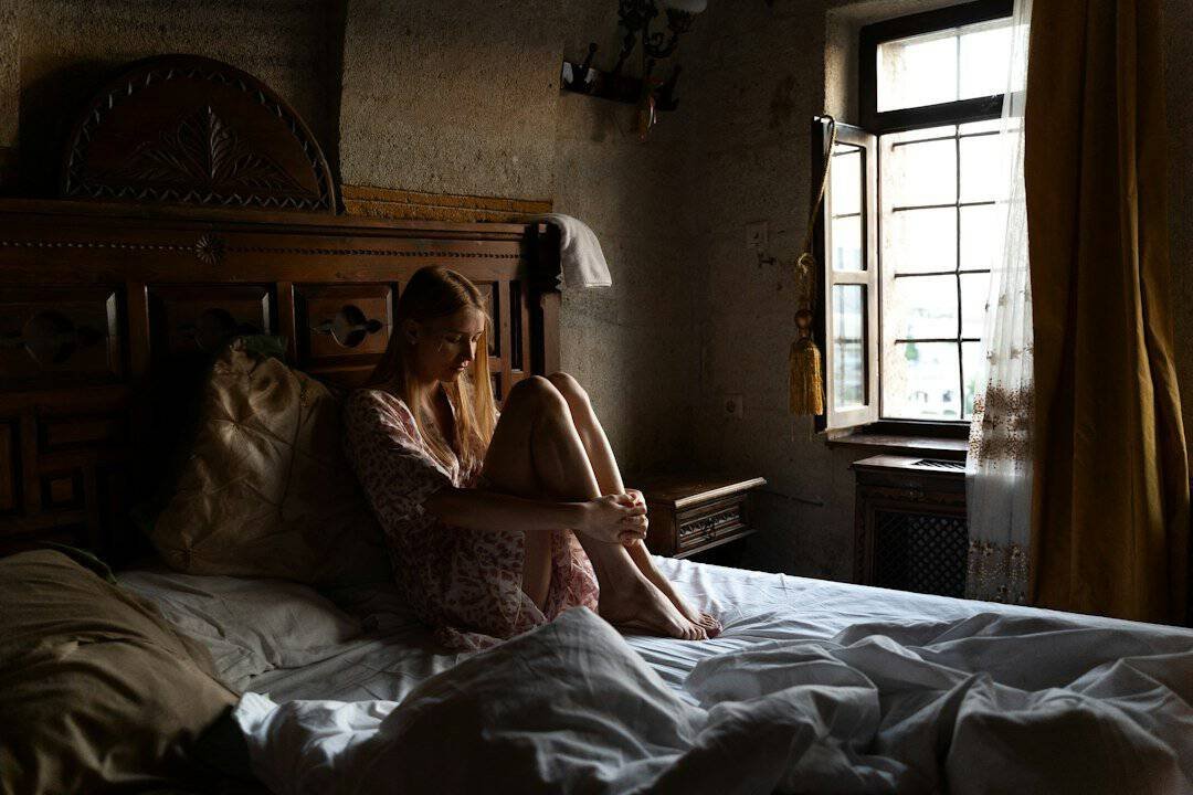 Moteris sėdi lovoje prie šviesaus lango ryte